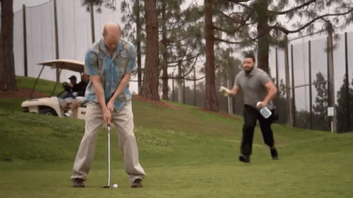 A Man In A Hawaiian Shirt Is Swinging A Golf Club On A Golf Course GIF