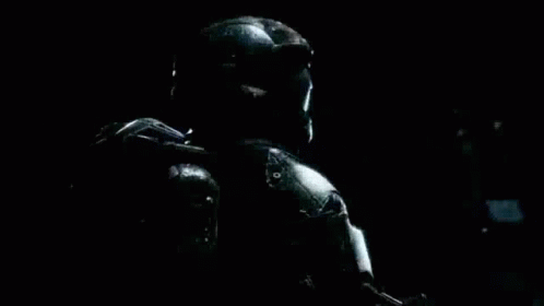 A Man In A Helmet And Armor Is Holding A Gun In A Dark Room . GIF
