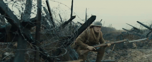 A Man In A Helmet Holding A Rifle In A Field GIF