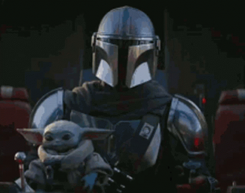 A Man In A Helmet Is Holding A Baby Yoda In His Lap . GIF
