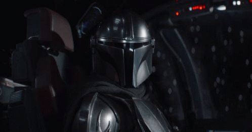A Man In A Helmet Is Sitting In A Dark Room And Says Grogu GIF