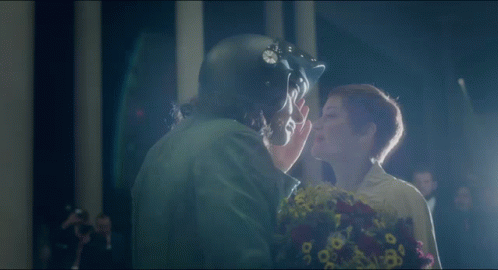 A Man In A Helmet Kisses A Woman With Flowers GIF