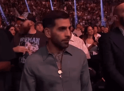 A Man In A Herman Shirt Stands In A Crowd Of People GIF