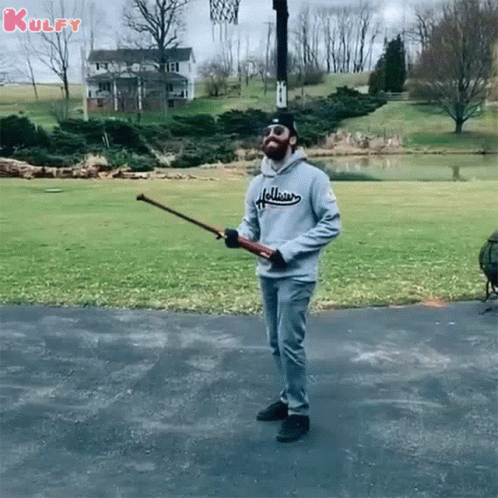A Man In A Hollister Sweatshirt Is Holding A Baseball Bat GIF