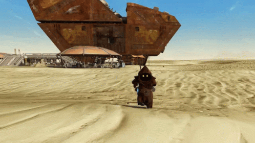 A Man In A Hood Is Walking In The Sand Near A Large Building GIF