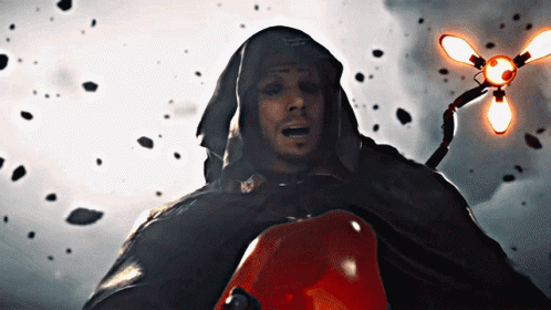 A Man In A Hooded Cape Holds A Red Object In His Hand GIF