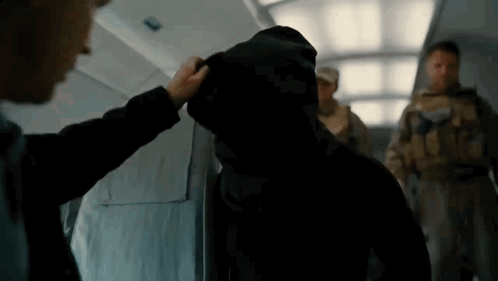 A Man In A Hooded Jacket Is Being Touched By Another Man GIF
