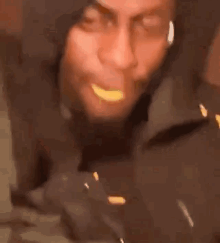 A Man In A Hooded Jacket Is Eating A Piece Of Food . GIF