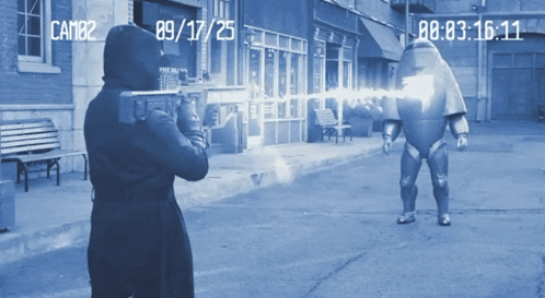 a man in a hooded jacket is holding a gun in front of a camera that says cam82 on the bottom