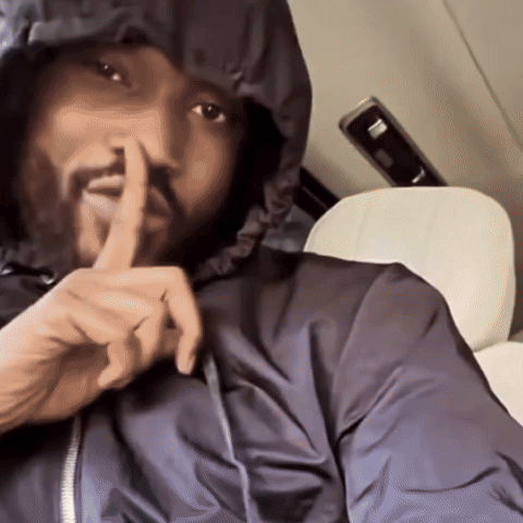 A Man In A Hooded Jacket Is Holding His Finger To His Mouth GIF
