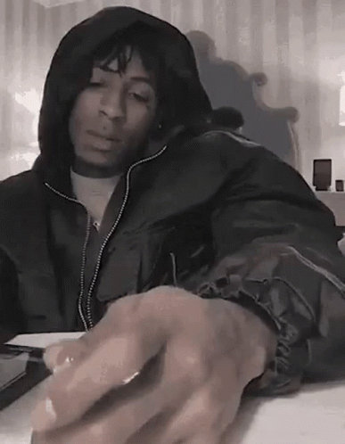 A Man In A Hooded Jacket Is Sitting At A Table With His Hands On The Keyboard . GIF
