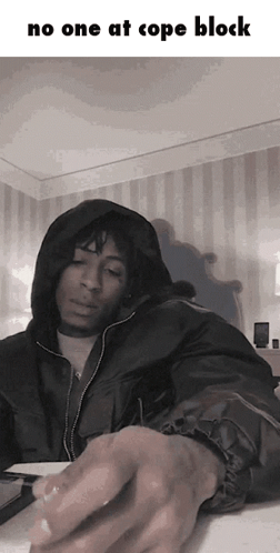 A Man In A Hooded Jacket Is Sitting At A Table With The Words No One At Cope Block Above Him GIF