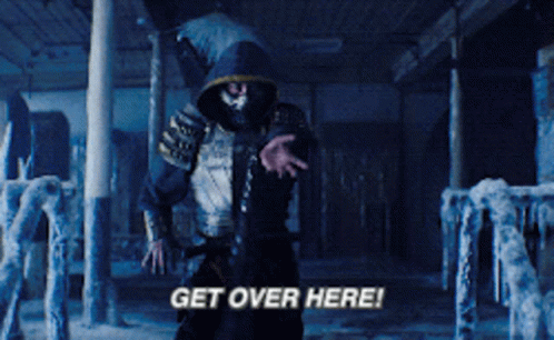 A Man In A Hooded Jacket Is Standing In A Dark Room And Says Get Over Here GIF