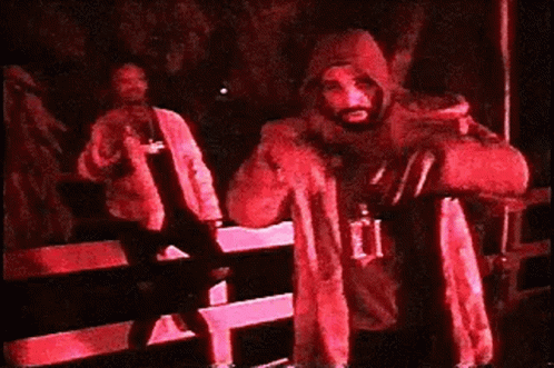 A Man In A Hooded Jacket Is Standing In A Dark Room Holding A Bag . GIF