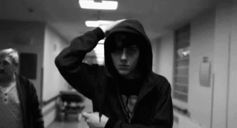 A Man In A Hooded Jacket Is Standing In A Hallway . GIF