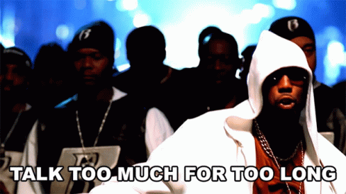 A Man In A Hooded Jacket Stands In Front Of A Crowd With The Words " Talk Too Much For Too Long " Below Him GIF