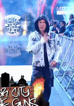 A Man In A Hooded Jacket Stands In Front Of A Sign That Says City Of Guns GIF
