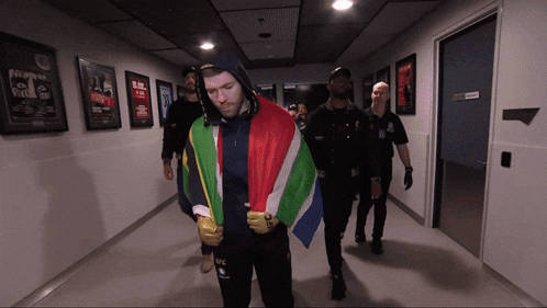 A Man In A Hooded Jacket With The Word Ufc On It Is Walking Down A Hallway GIF