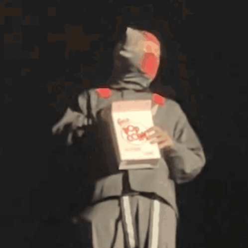 A Man In A Hooded Sweatshirt Is Holding A Box Of Nacho Cheese .. GIF