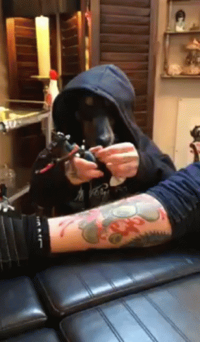 A Man In A Hoodie Is Getting A Tattoo On Another Man 'S Arm GIF