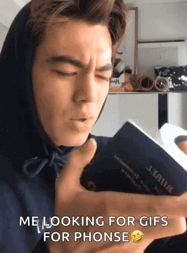 A Man In A Hoodie Is Holding A Book That Says Me Looking For Gifs For Phones GIF