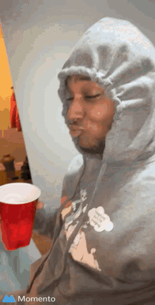 A Man In A Hoodie Is Holding A Red Cup In His Hand . GIF