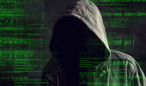 a man in a hoodie is sitting at a table with a laptop computer .