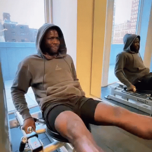 A Man In A Hoodie Is Sitting On A Machine In Front Of A Mirror . GIF