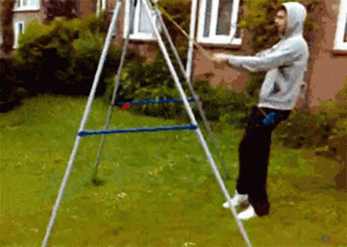 A Man In A Hoodie Is Standing In Front Of A Swing Set In A Yard GIF