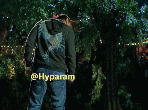 A Man In A Hoodie Is Standing In Front Of A Tree With The Word Hyparam On The Bottom Right Corner GIF