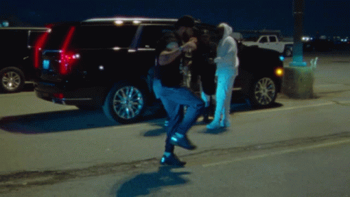 A Man In A Hoodie Stands In Front Of A Black Suv GIF