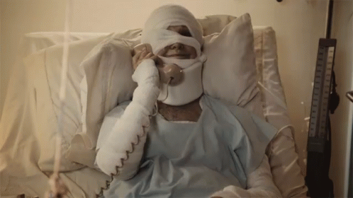 A Man In A Hospital Bed With A Bandaged Head Talking On A Phone GIF