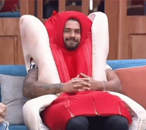 A Man In A Hot Dog Costume Is Sitting On A Couch With His Legs Crossed . GIF