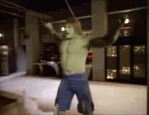 A Man In A Hulk Costume Is Standing In A Room With His Arms Outstretched And Holding A Stick . GIF