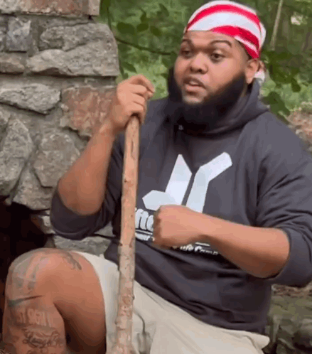 A Man In A Hurley Sweatshirt Holds A Wooden Stick GIF