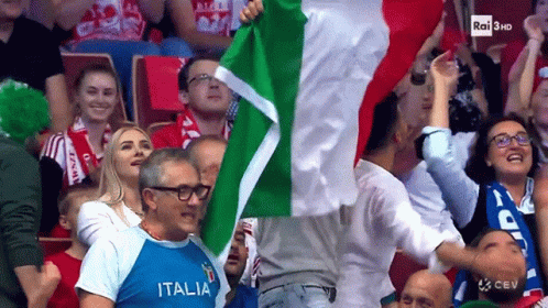 A Man In A Italia Shirt Is Holding A Flag In A Crowd GIF