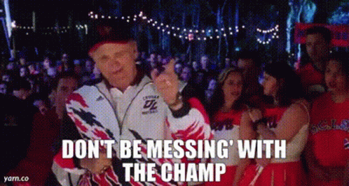 A Man In A Jacket Is Standing In Front Of A Crowd Of People And A Cheerleader . GIF