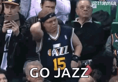 A Man In A Jazz Jersey Is Sitting In The Stands Watching A Basketball Game And Says `` Go Jazz '' . GIF