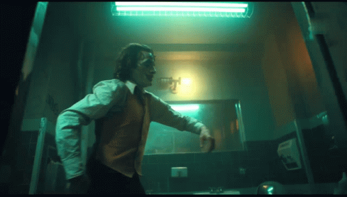 A Man In A Joker Costume Is Standing In A Dark Room GIF