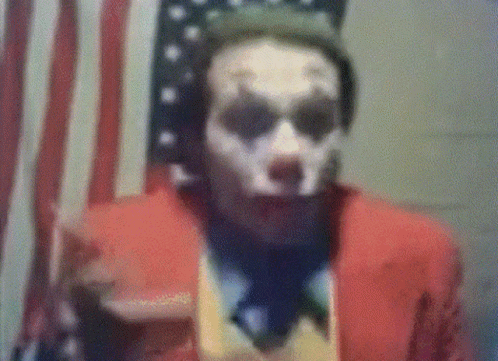 A Man In A Joker Costume Is Standing In Front Of An American Flag . GIF