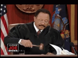 A Man In A Judge 'S Robe Is Holding A Gavel In Front Of A Sign That Says Judge Joe Brown GIF