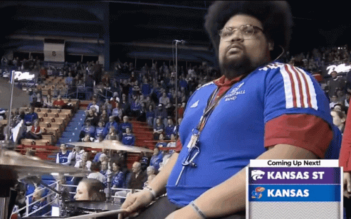 A Man In A Kansas Shirt Is Playing Drums In Front Of A Crowd GIF