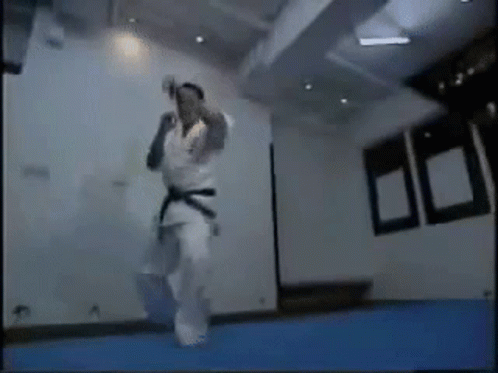 A Man In A Karate Uniform Is Jumping In The Air In A Room . GIF