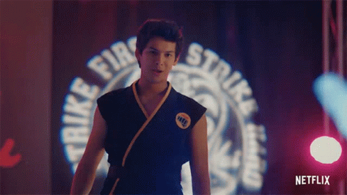A Man In A Karate Uniform Is Standing In Front Of A Sign That Says Strike Fire Strike . GIF