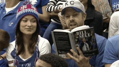 A Man In A Kc Hat Is Reading A Book By Bill Self GIF