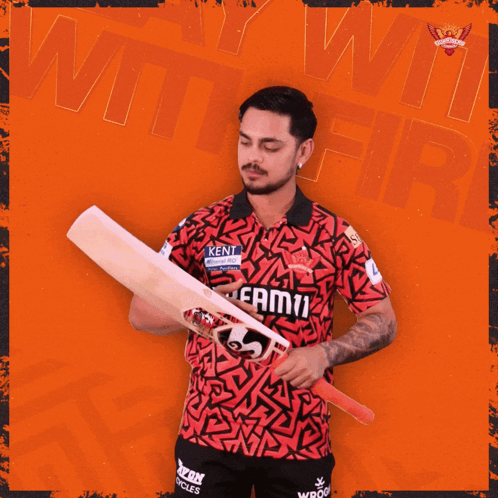 a man in a kent shirt holds a cricket bat in front of an orange background