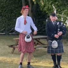 A Man In A Kilt Is Playing A Bagpipe Next To Another Man In A Kilt GIF