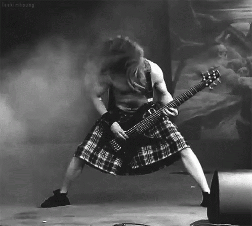 A Man In A Kilt Is Playing A Guitar In A Black And White Photo GIF