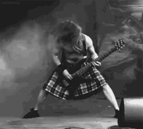 A Man In A Kilt Is Playing A Guitar On Stage In A Black And White Photo . GIF