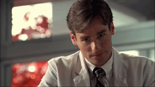 A Man In A Lab Coat And Tie Is Looking Down GIF